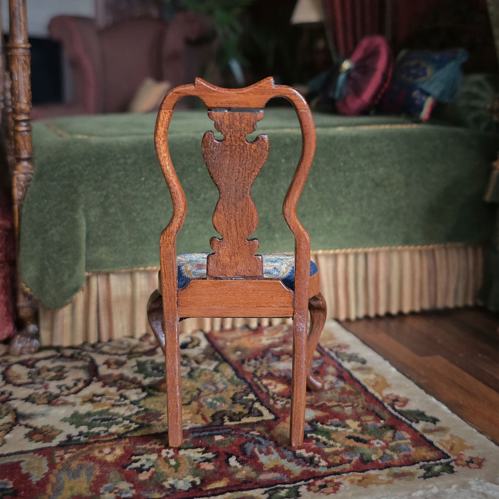 Wooden chair with intricately carved wood backrest on a patterned rug in a room with green bed and colorful decor.