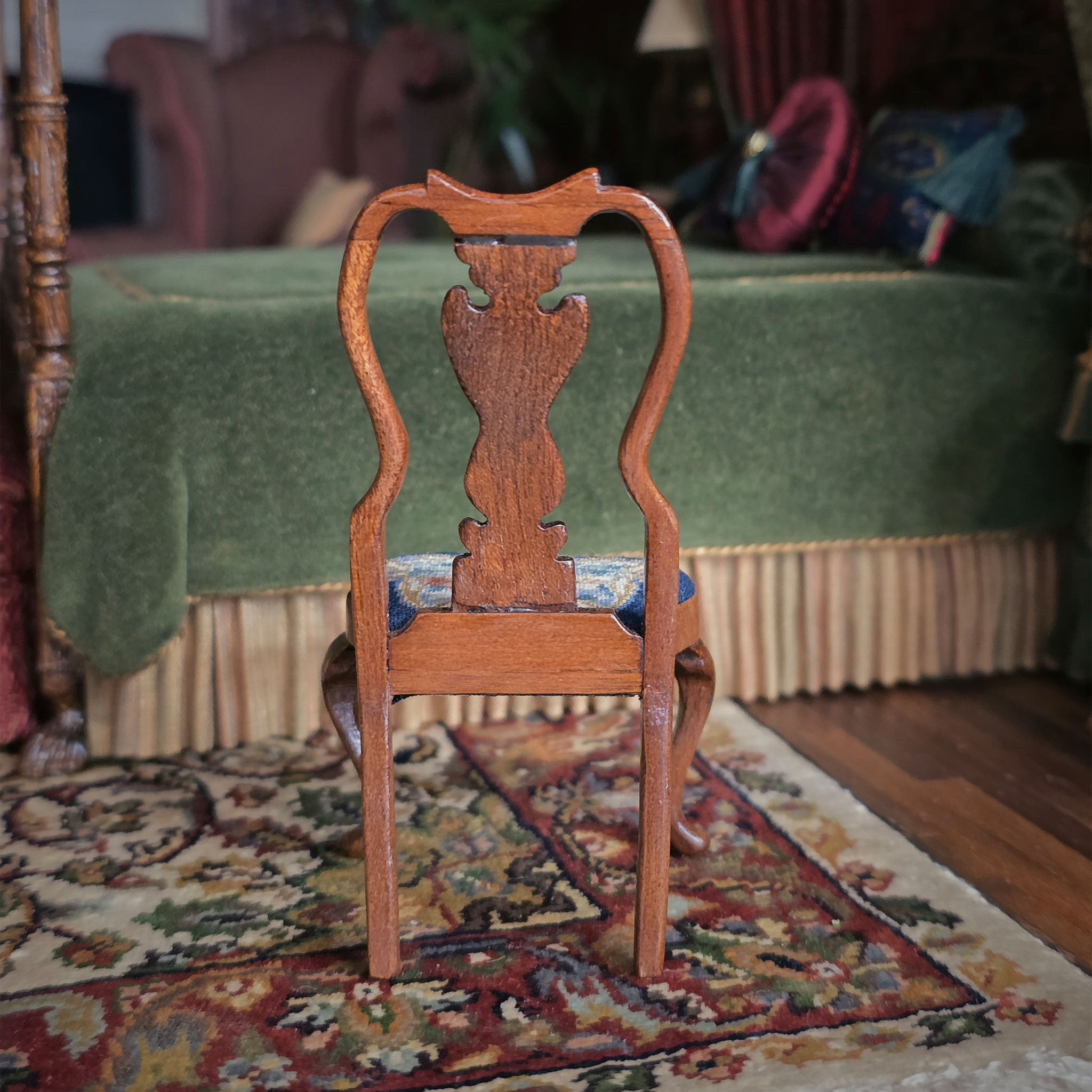 Wooden chair with intricately carved wood backrest on a patterned rug in a room with green bed and colorful decor.