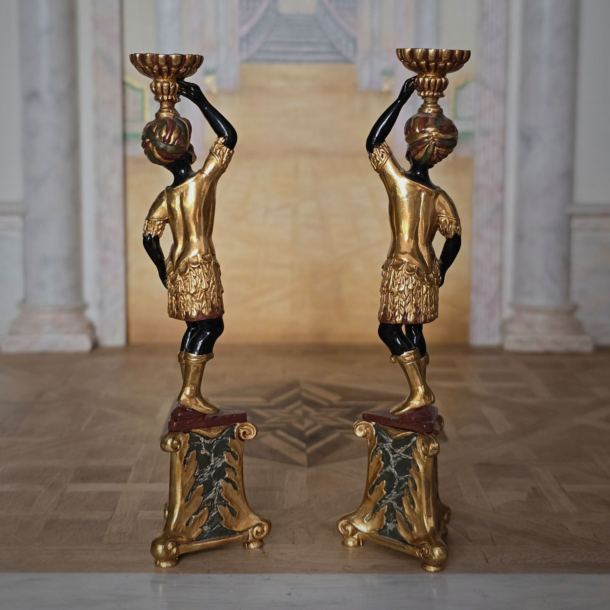 Pair of ornate pedestals with gold and black finish in a classical setting.