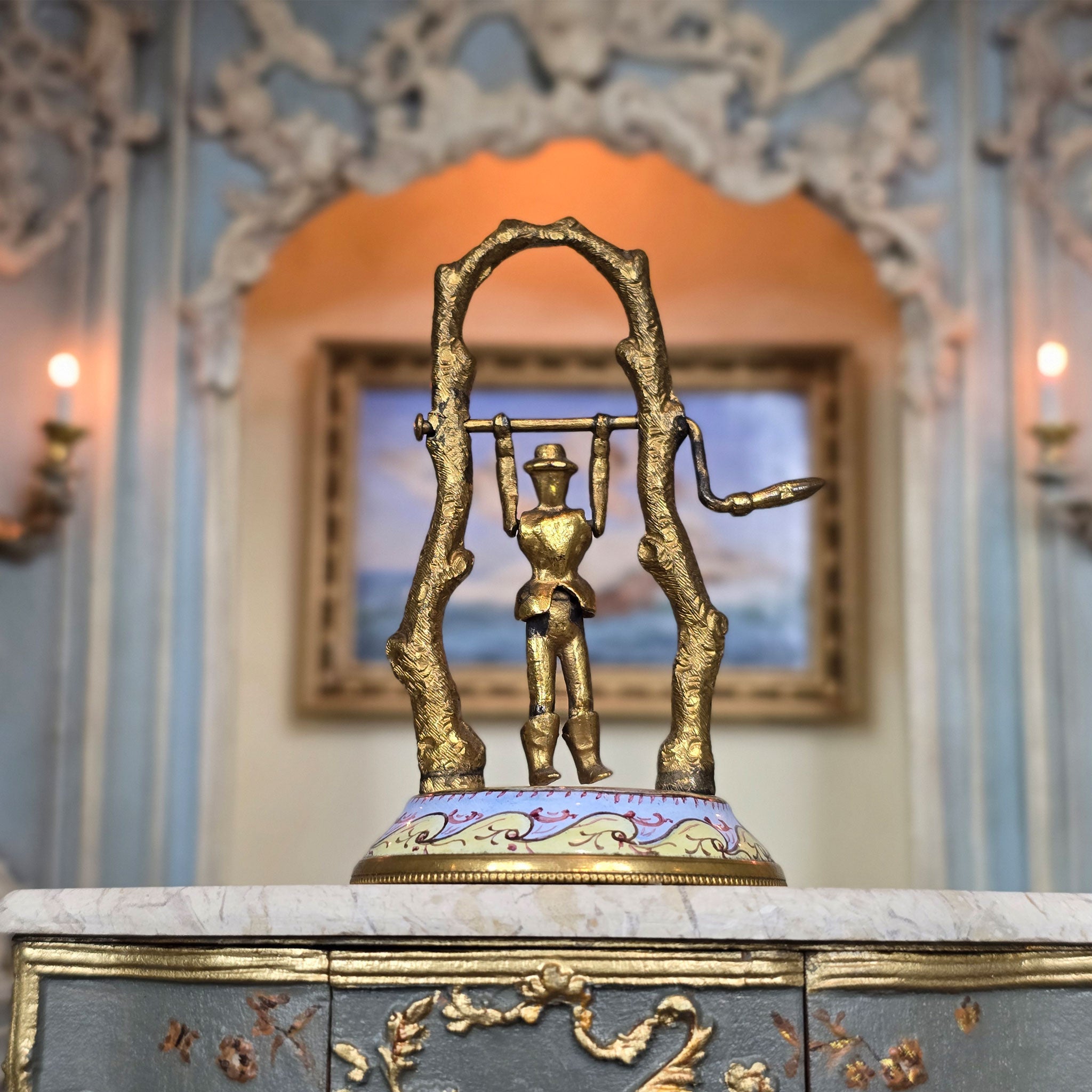 Decorative gold automata children's toy in miniature on a marble surface with an ornate wall in the background