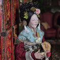 Load image into Gallery viewer, Traditional doll in intricate costume with decorative hairpiece and fan, standing next to a wooden cabinet.
