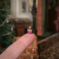 Load image into Gallery viewer, Small purple and gold decorative ornament held between fingers with a blurred festive background
