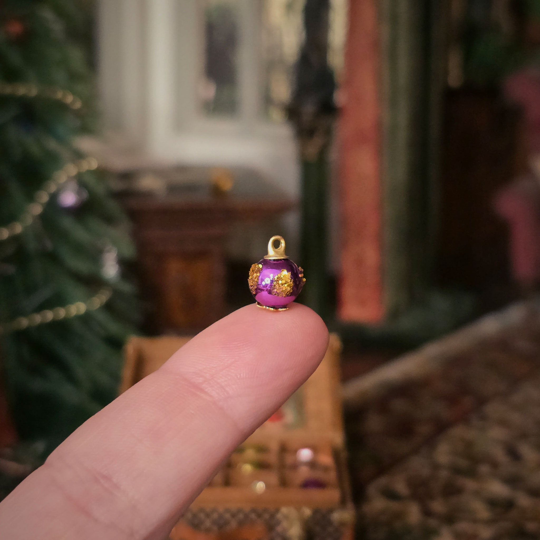 Small purple and gold decorative ornament held between fingers with a blurred festive background