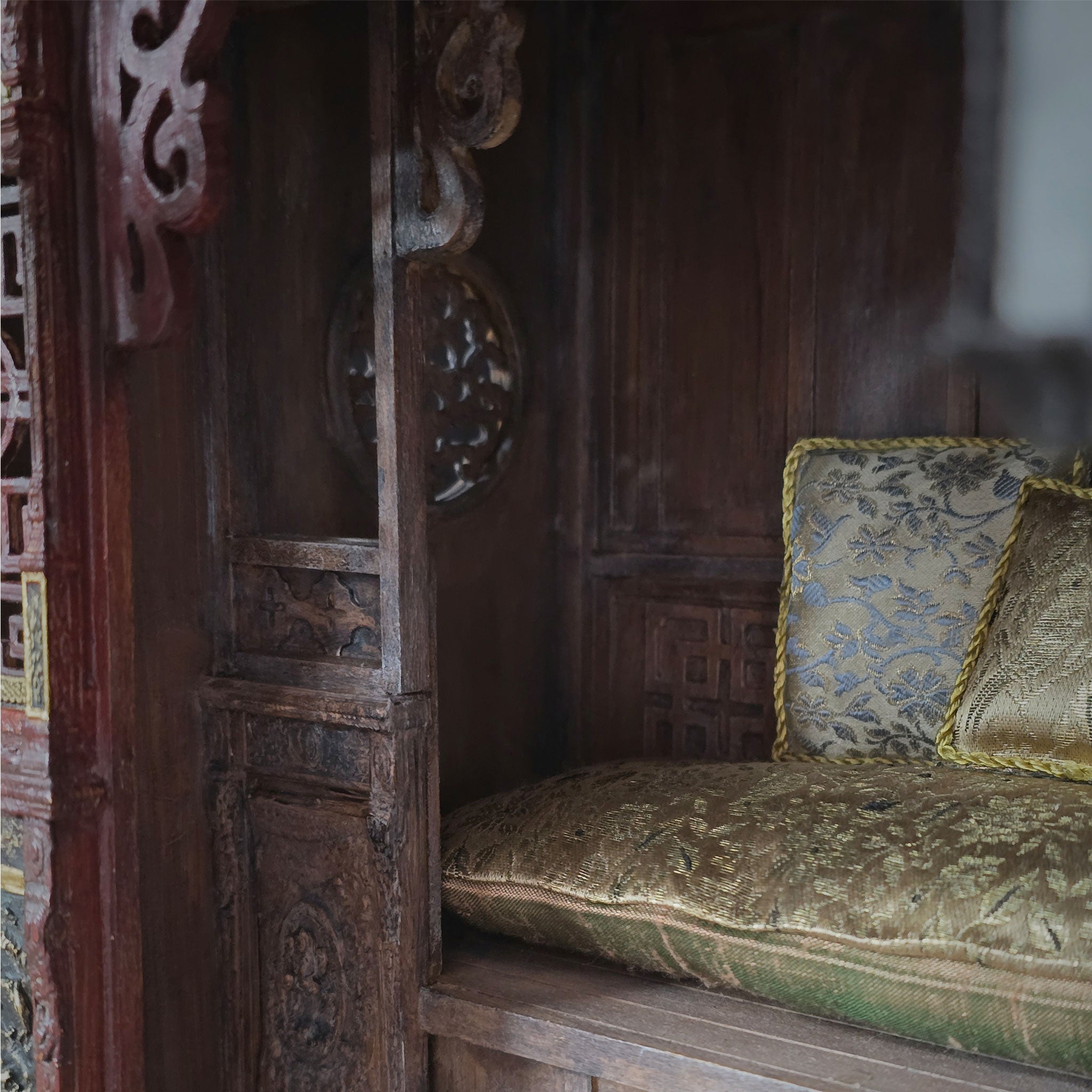 Decorative wooden seat with ornate cushions in a traditional opium wedding bed setting