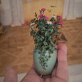 Load image into Gallery viewer, Small green planter with flowers held in a hand against a blurred indoor background
