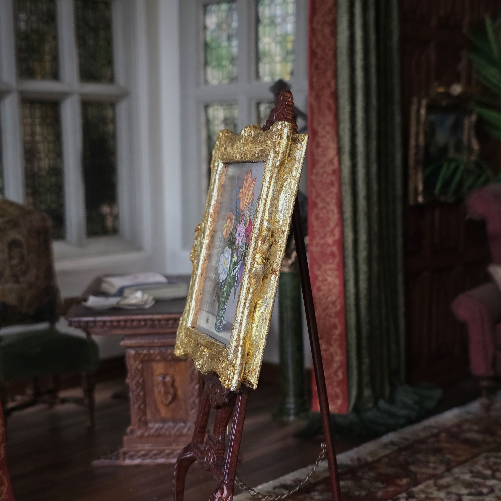 Decorative painting on a gold easel in an elegant room with furniture and a window.