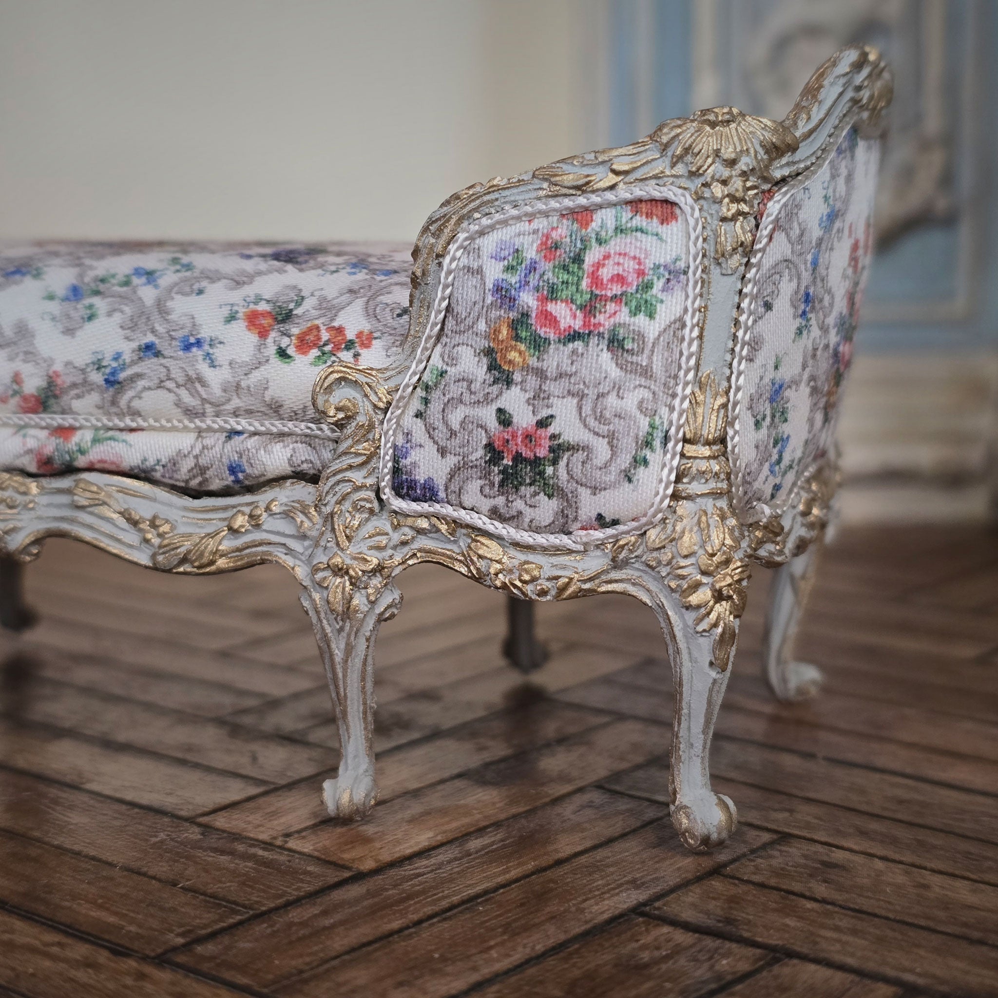 Decorative floral-patterned chaise with gold accents on a wooden floor.