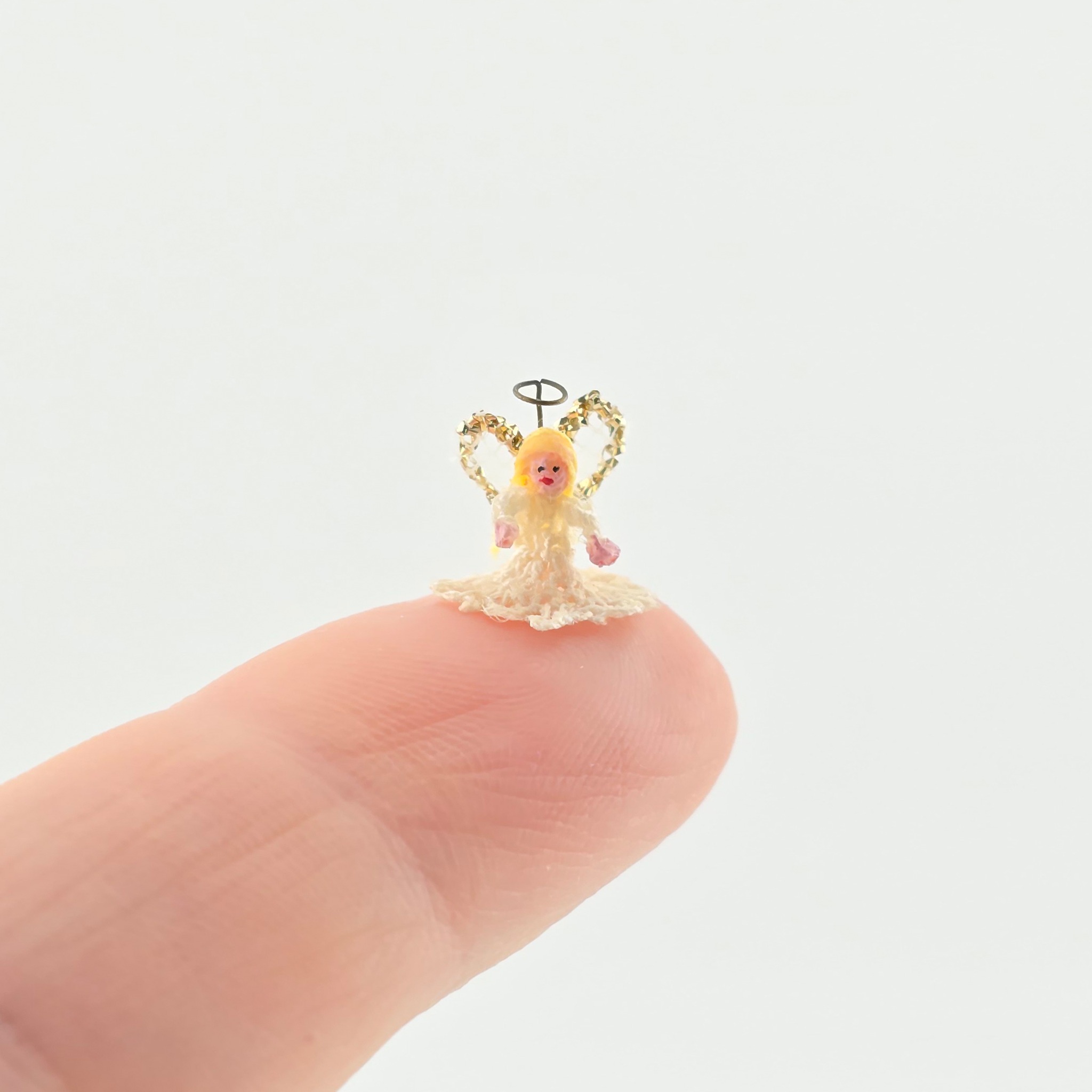 tiny angel tree topper for Christmas on finger on a white background