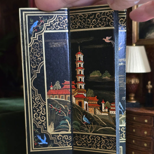 Decorative book with intricate illustrations of a tower and nature, held open by a hand.