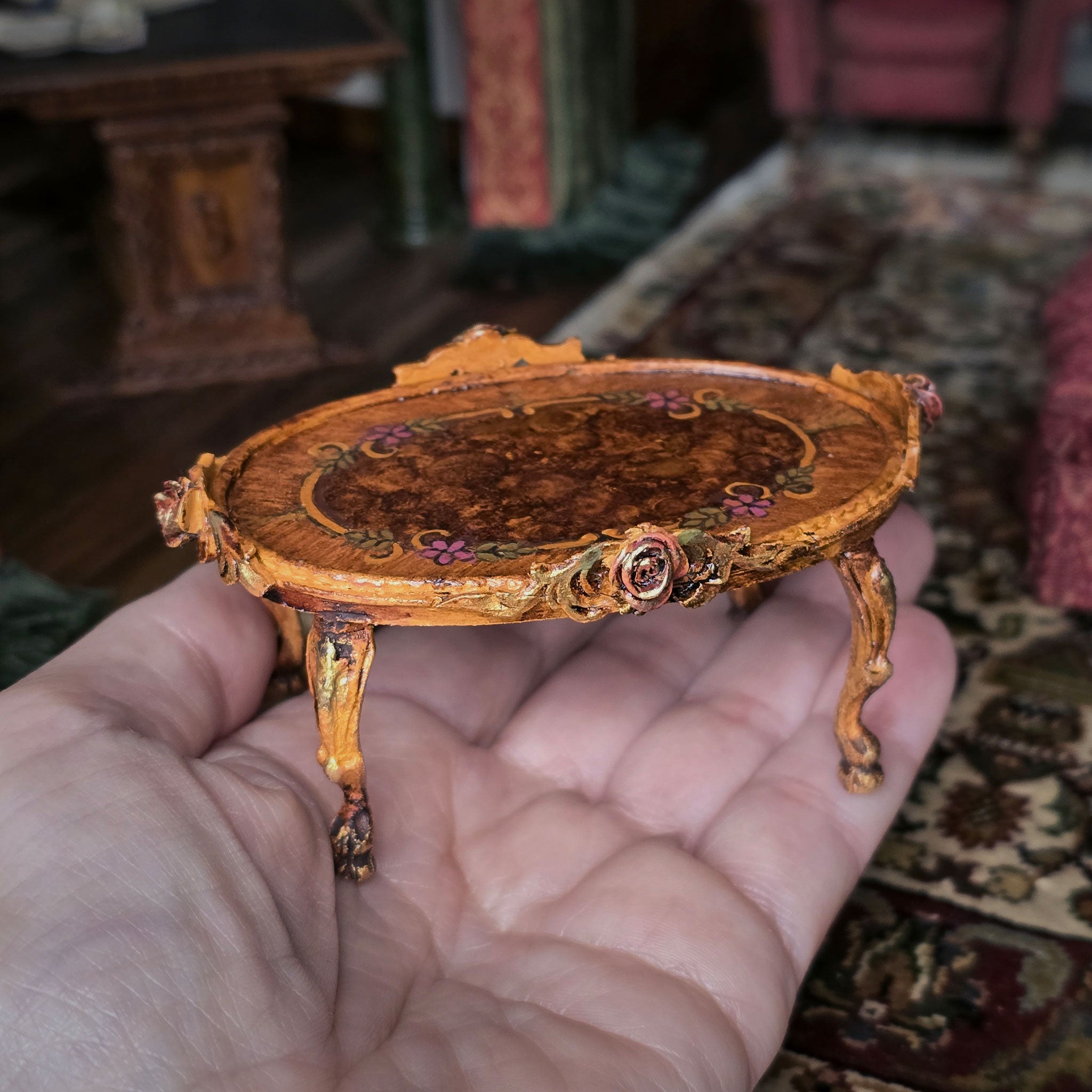 Miniature ornate table held in a hand with a blurred indoor setting