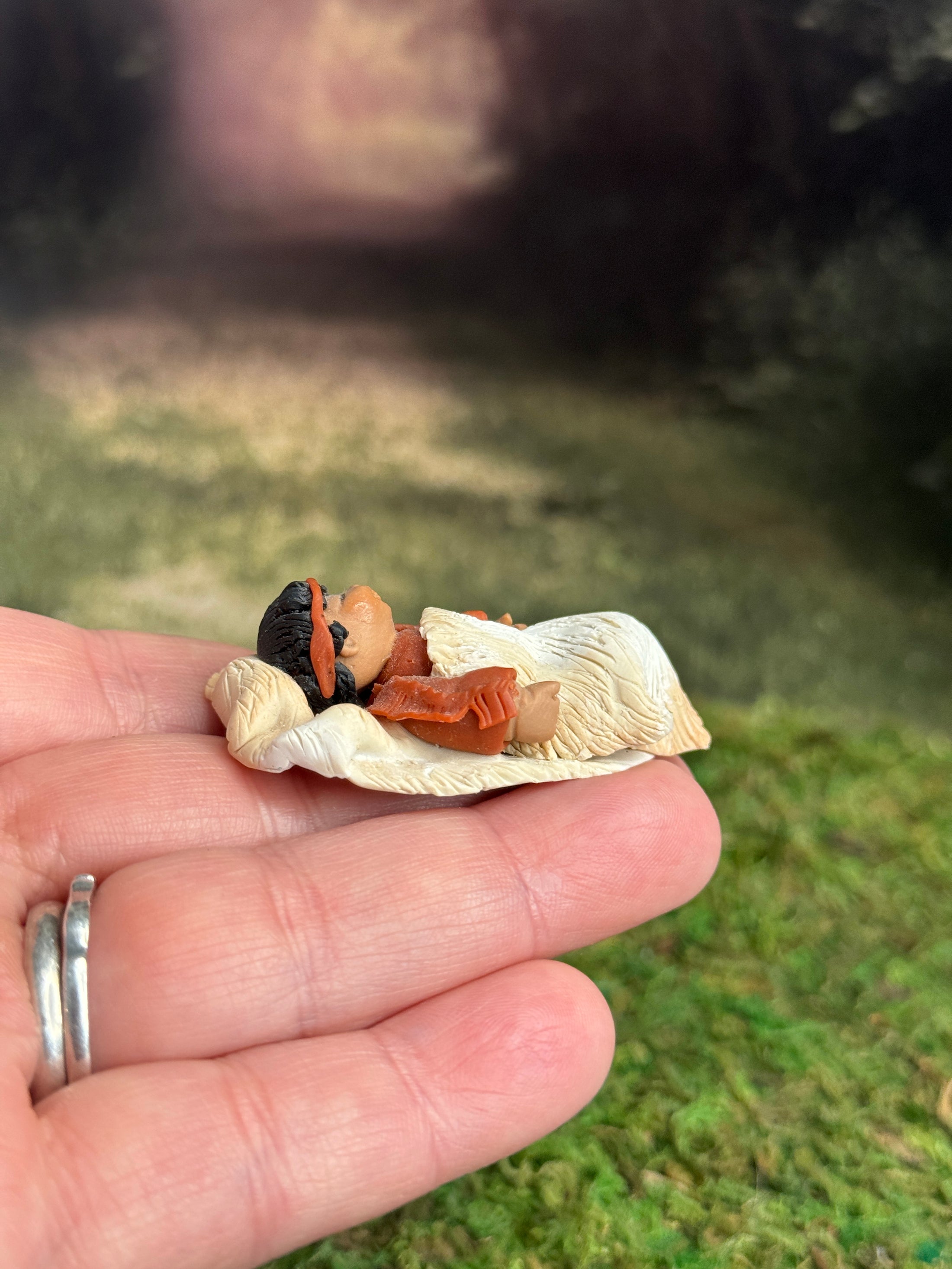 Signed Sculpted Clay Sleeping Native American Baby Doll Figurine, laying in a hand, right side view