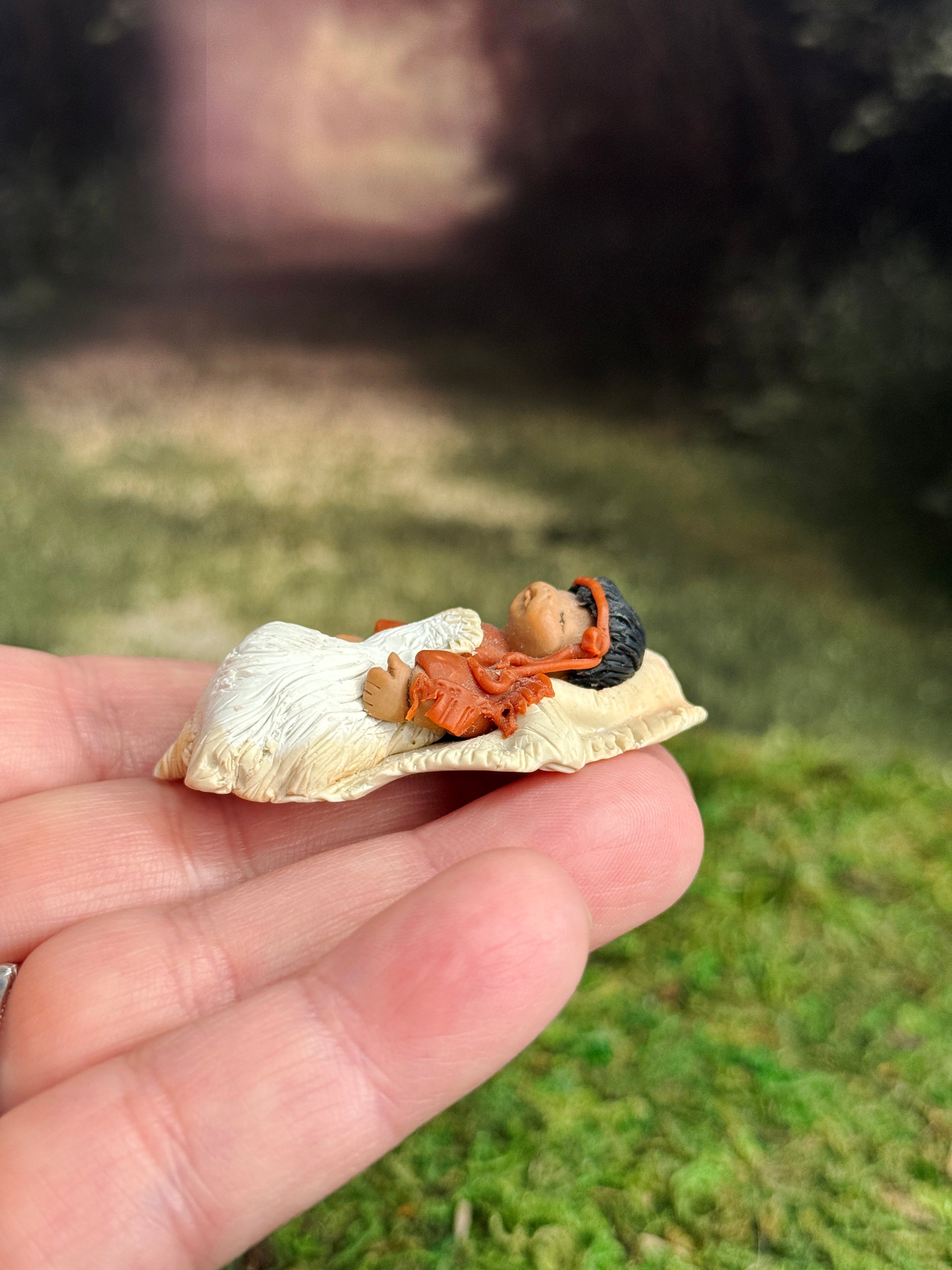 Signed Sculpted Clay Sleeping Native American Baby Doll Figurine, laying in a hand, left side view