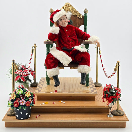 Santa Claus dollhouse doll sitting in a chair with Christmas decorations around.
