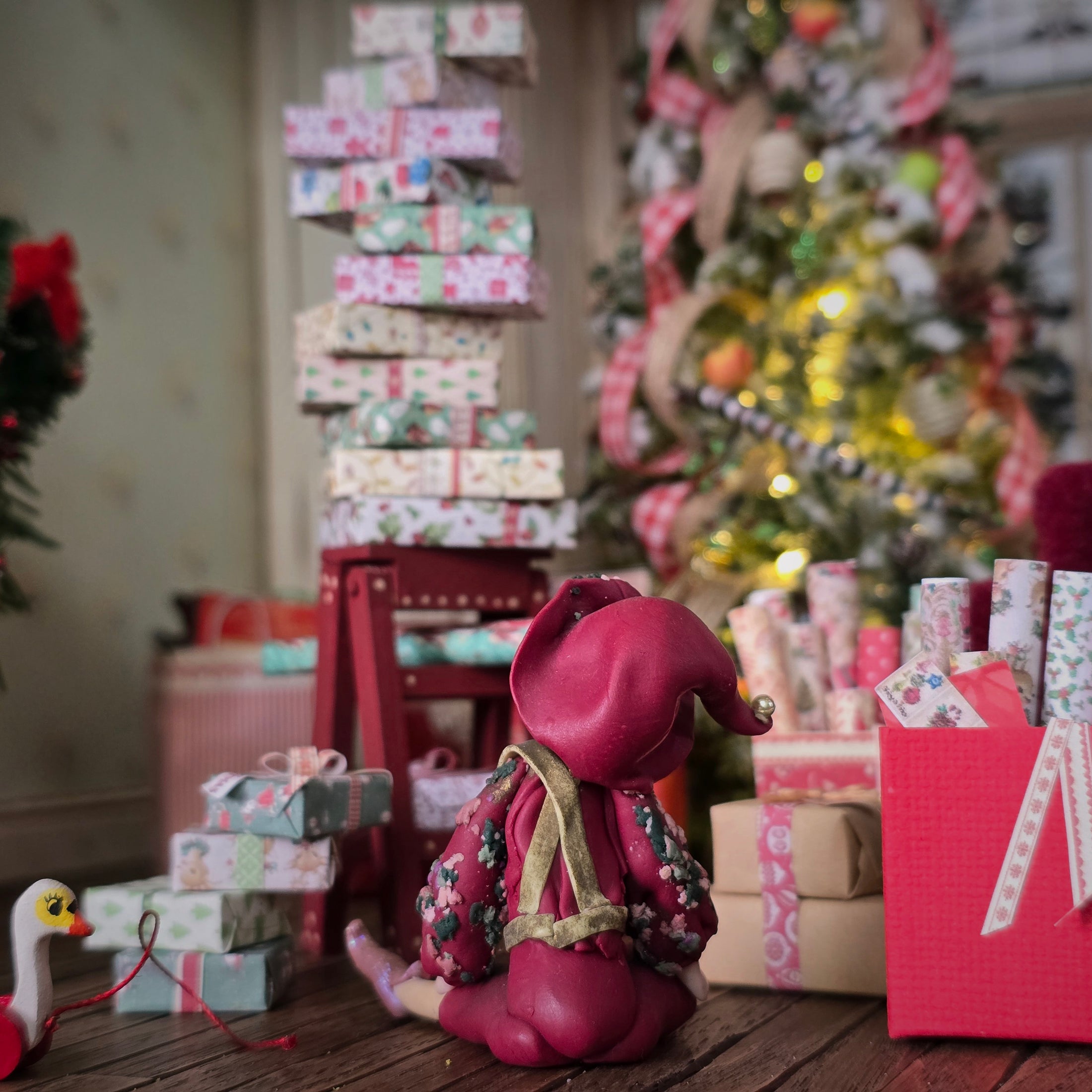 back view of a Hand-Sculpted Clay Elf Boy in Raspberry Pink in a festive setting with Christmas tree and presents.