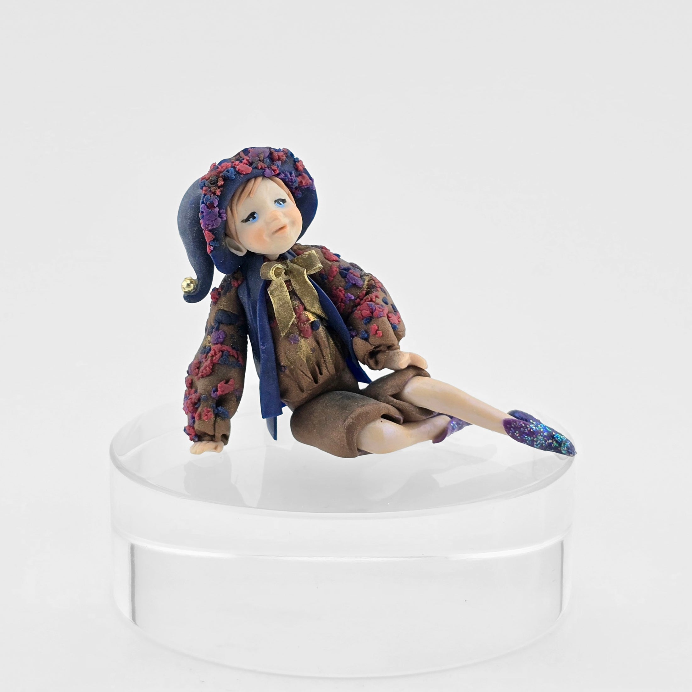 Sculpted clay elf boy doll wearing a purple outfit on a white background
