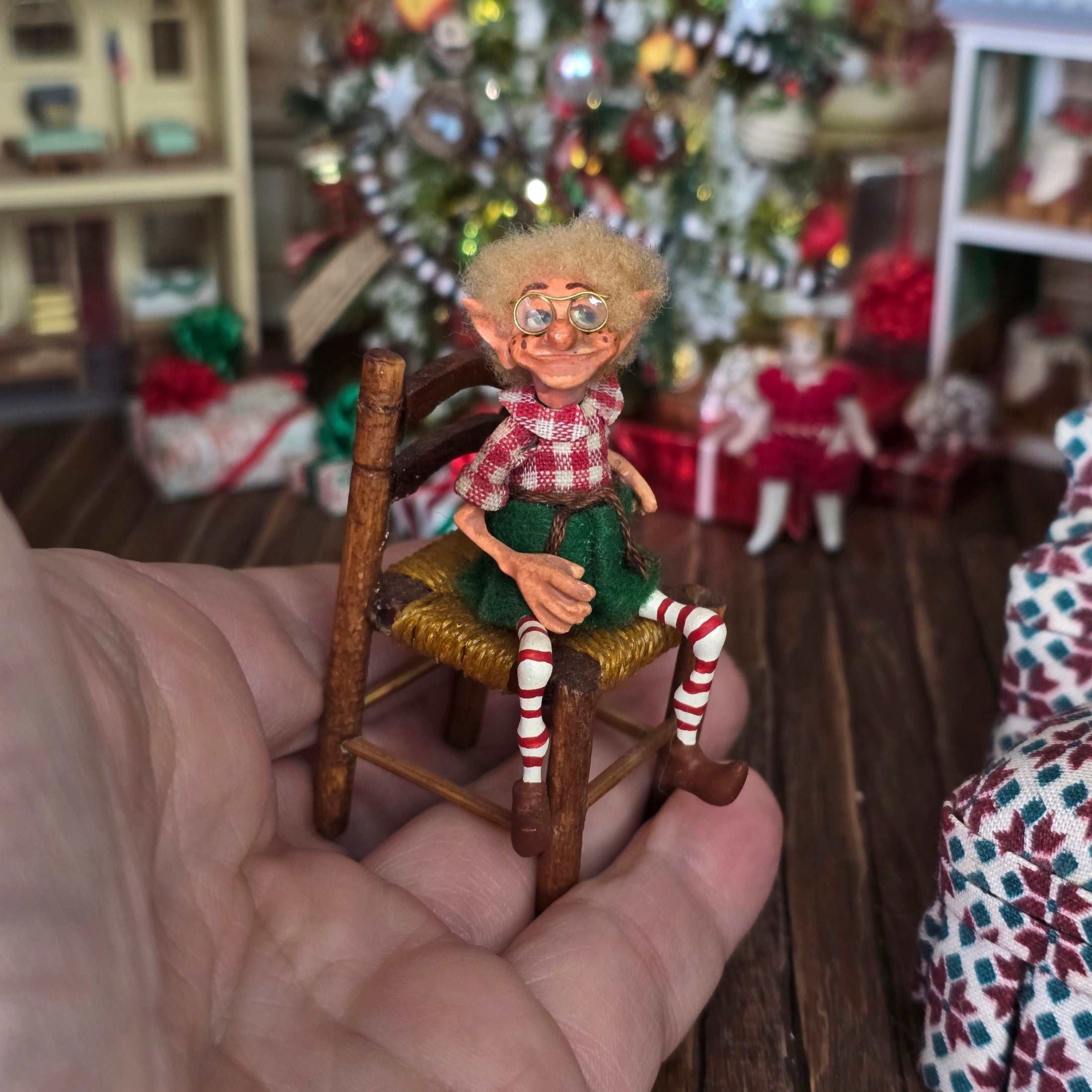 Christmas elf with glasses by artist Cynthia Baron, in chair, held in a hand