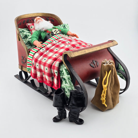 Sleeping miniature dollhouse santa in bed with his boots and toy bag