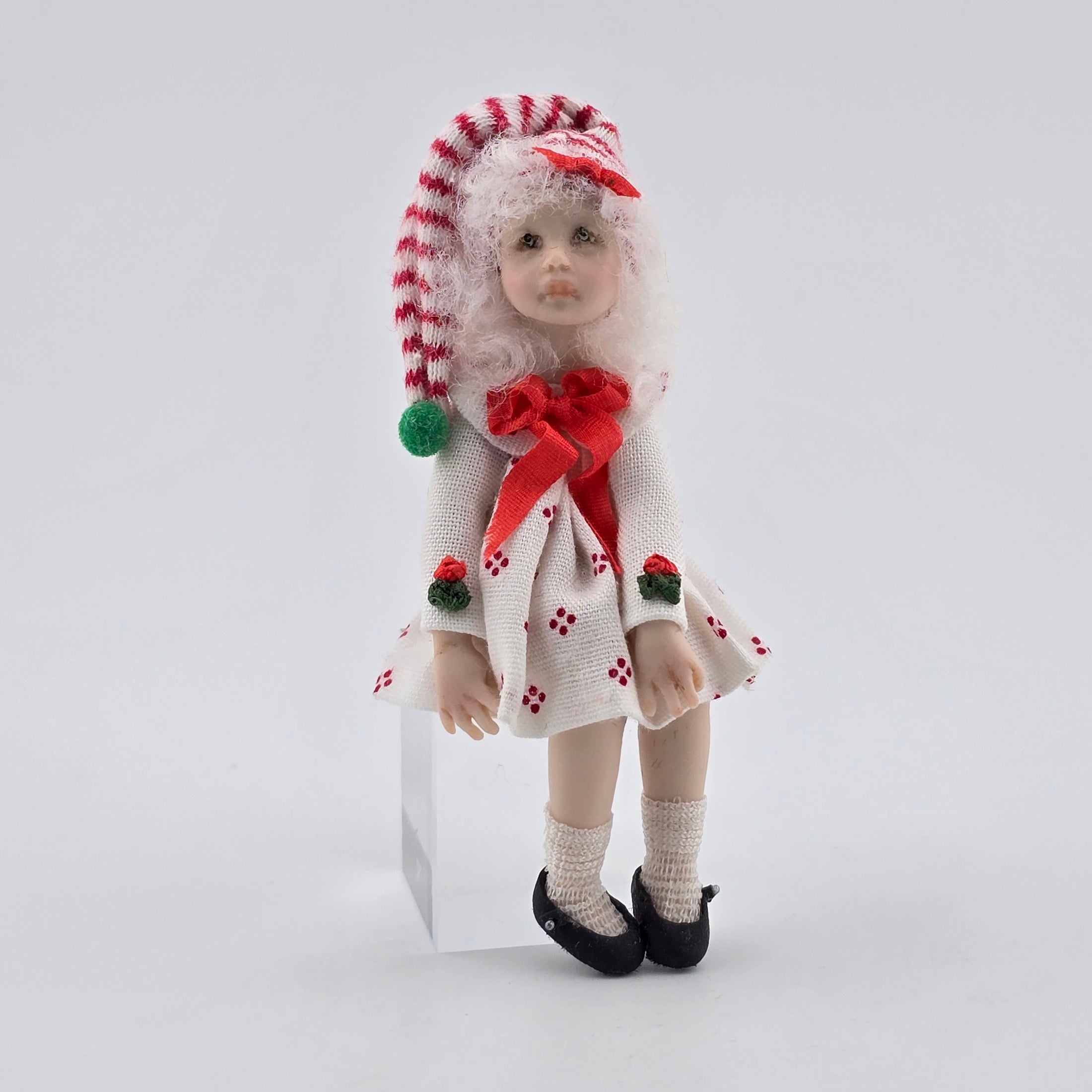  Christmas girl doll by artisan Carol McBride wearing a festive outfit with a red bow and candy cane hat on a white background