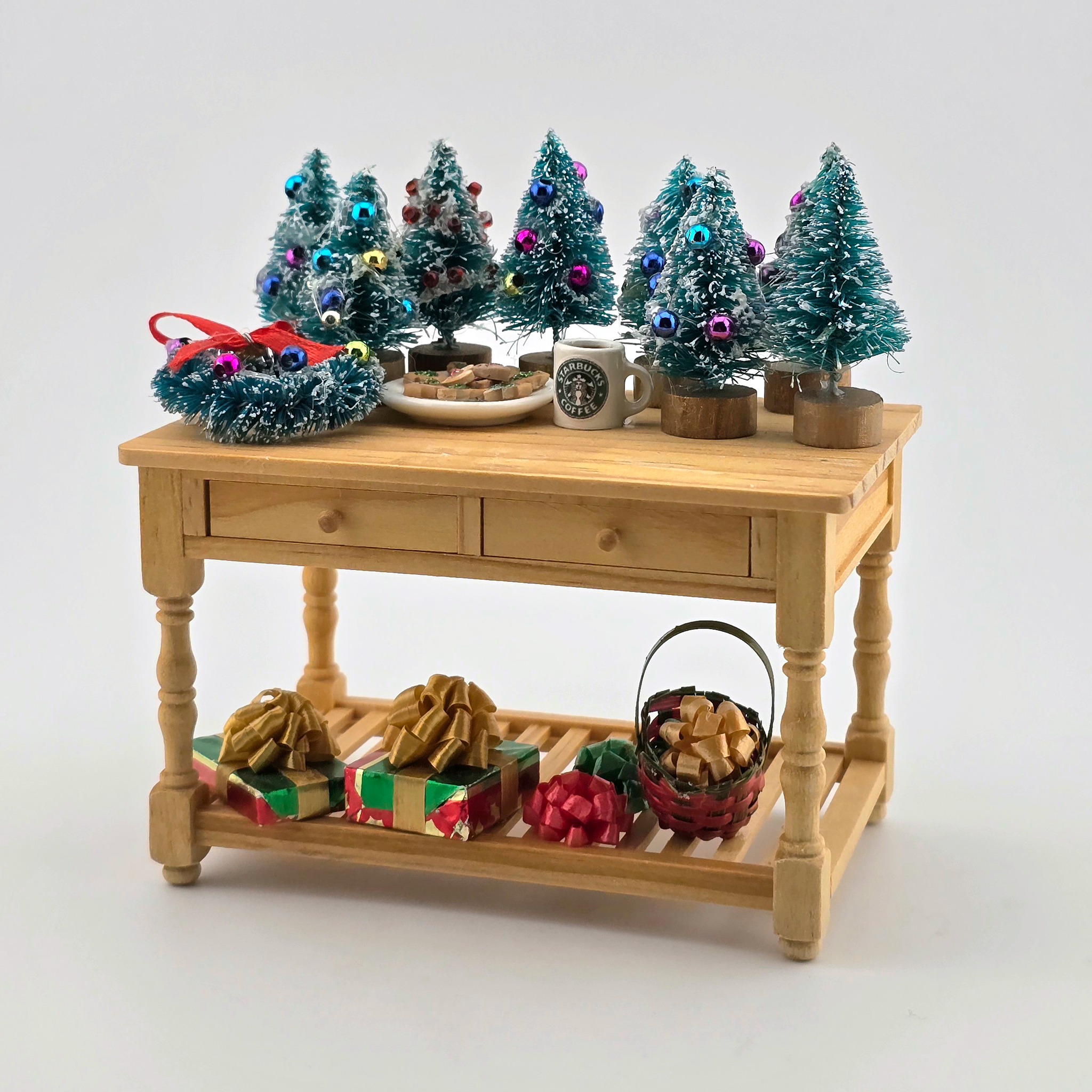 Wooden table with miniature Christmas trees, wreaths, and gift boxes on a white background