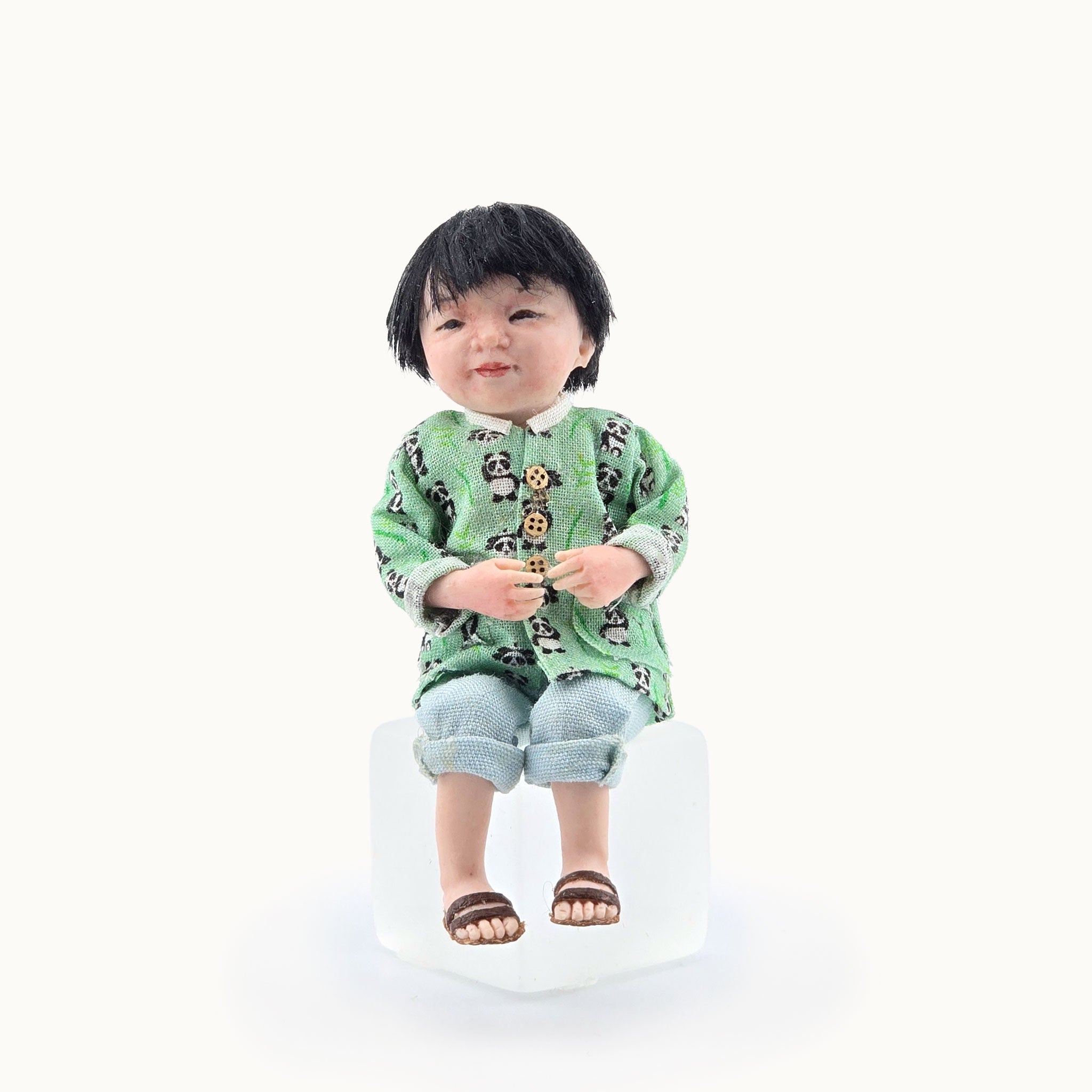 Miniature Chinese dollhouse character doll by Svetlana Blasing, wearing a green patterned panda shirt on a white background