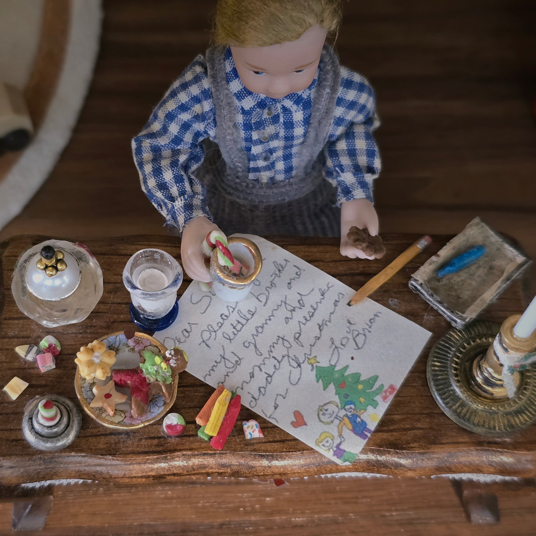 Miniature doll in a checkered shirt with a letter and cookies on a wooden table
