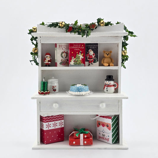 Decorative shelf with Christmas-themed items including books, a teddy bear, and small figurines on a white background.