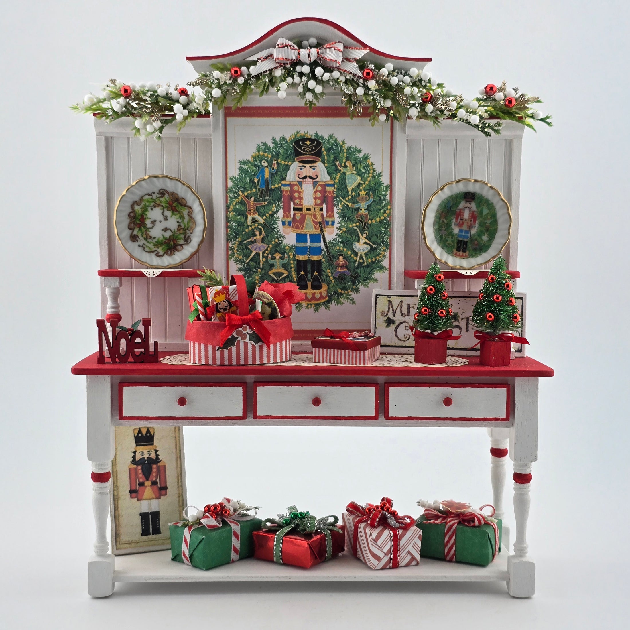 Decorative Christmas-themed cabinet with wreaths, nutcrackers, and gift boxes on a white background