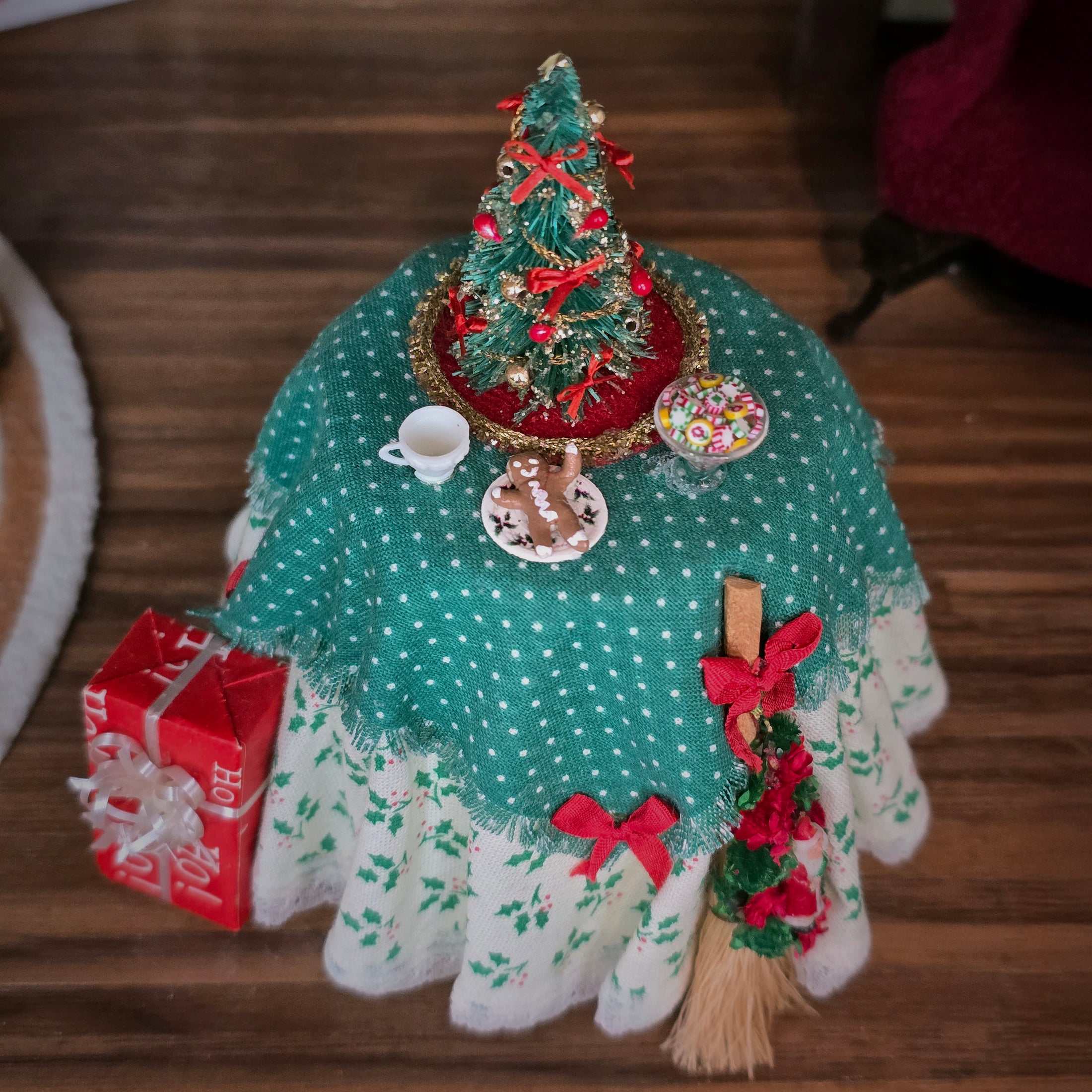 Decorative Christmas tablecloth with a small tree, presents, and other ornaments on a wooden surface.