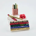 Load image into Gallery viewer, Stack of patterned miniature rolls of wrapping paper with a red bow on a white background

