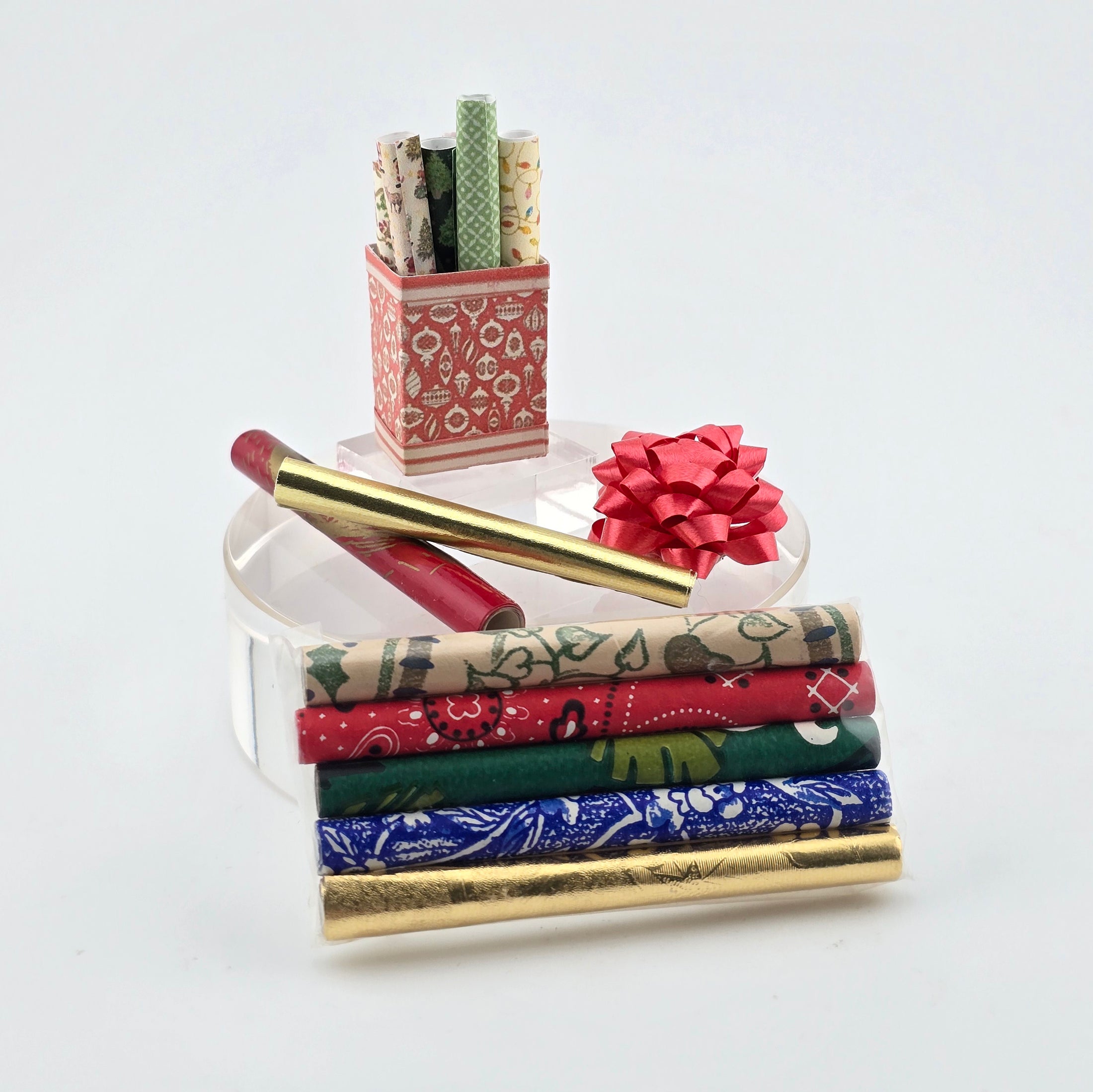 Stack of patterned miniature rolls of wrapping paper with a red bow on a white background