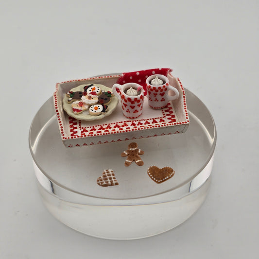 Miniature Christmas scene with cups, cookies, and a box on a white surface