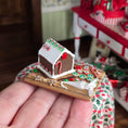 Load image into Gallery viewer, Miniature gingerbread house on a wooden base held in a hand with a blurred festive background.
