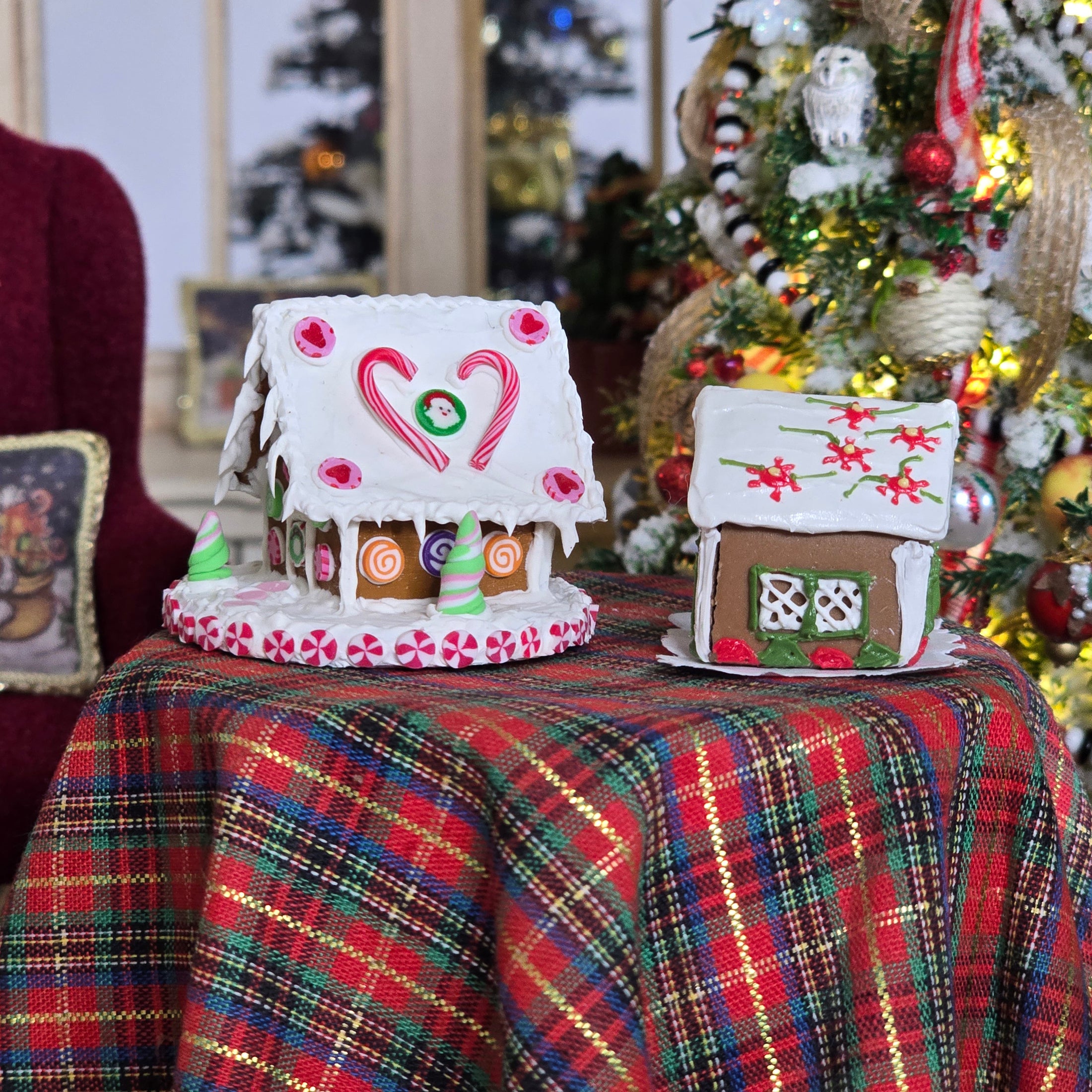 Decorative gingerbread houses on a plaid tablecloth with Christmas trees in the background