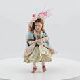 Load and play video in Gallery viewer, Seated Porcelain Little Girl Doll with Teacup, Pink Feathered Hat & Leather Shoes
