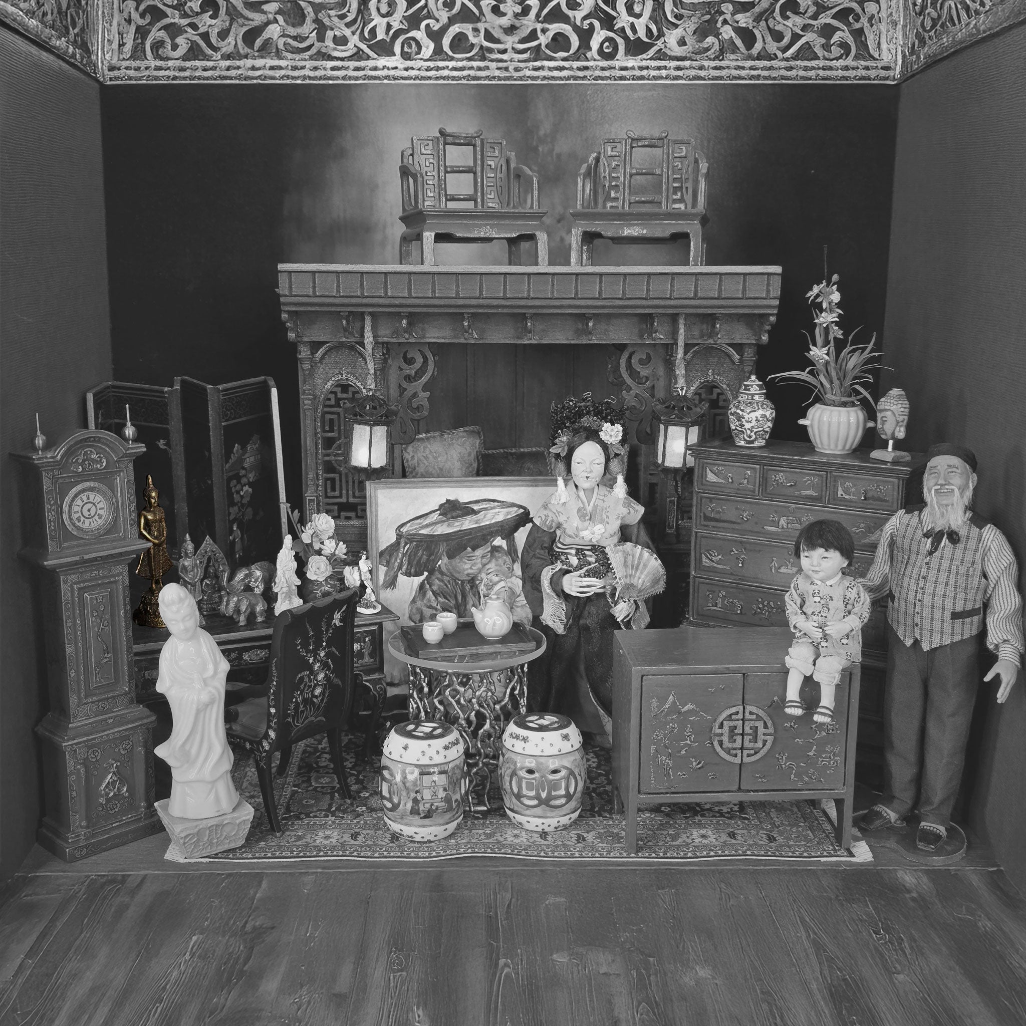 Black and white miniature dollhouse scene with furniture and figures.