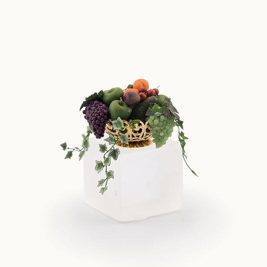 Decorative miniature dollhouse arrangement of fruits and ivy in a brass bowl on a white background