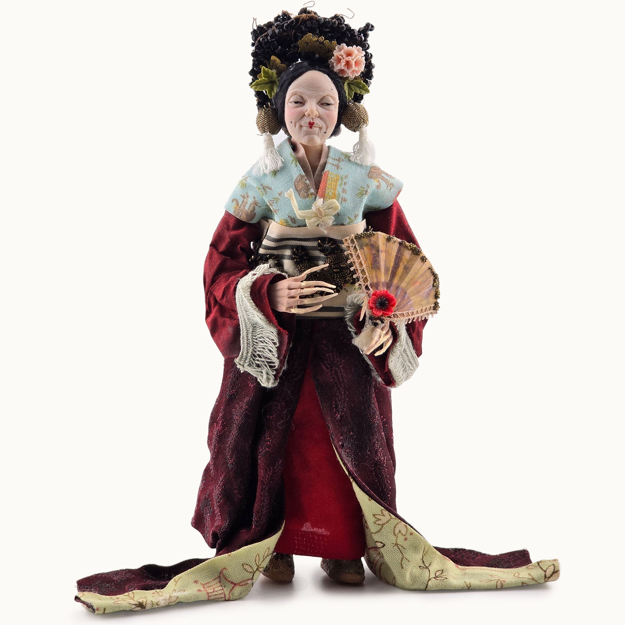 Traditional Japanese doll in elaborate kimono with fan and flower accessories on a white background