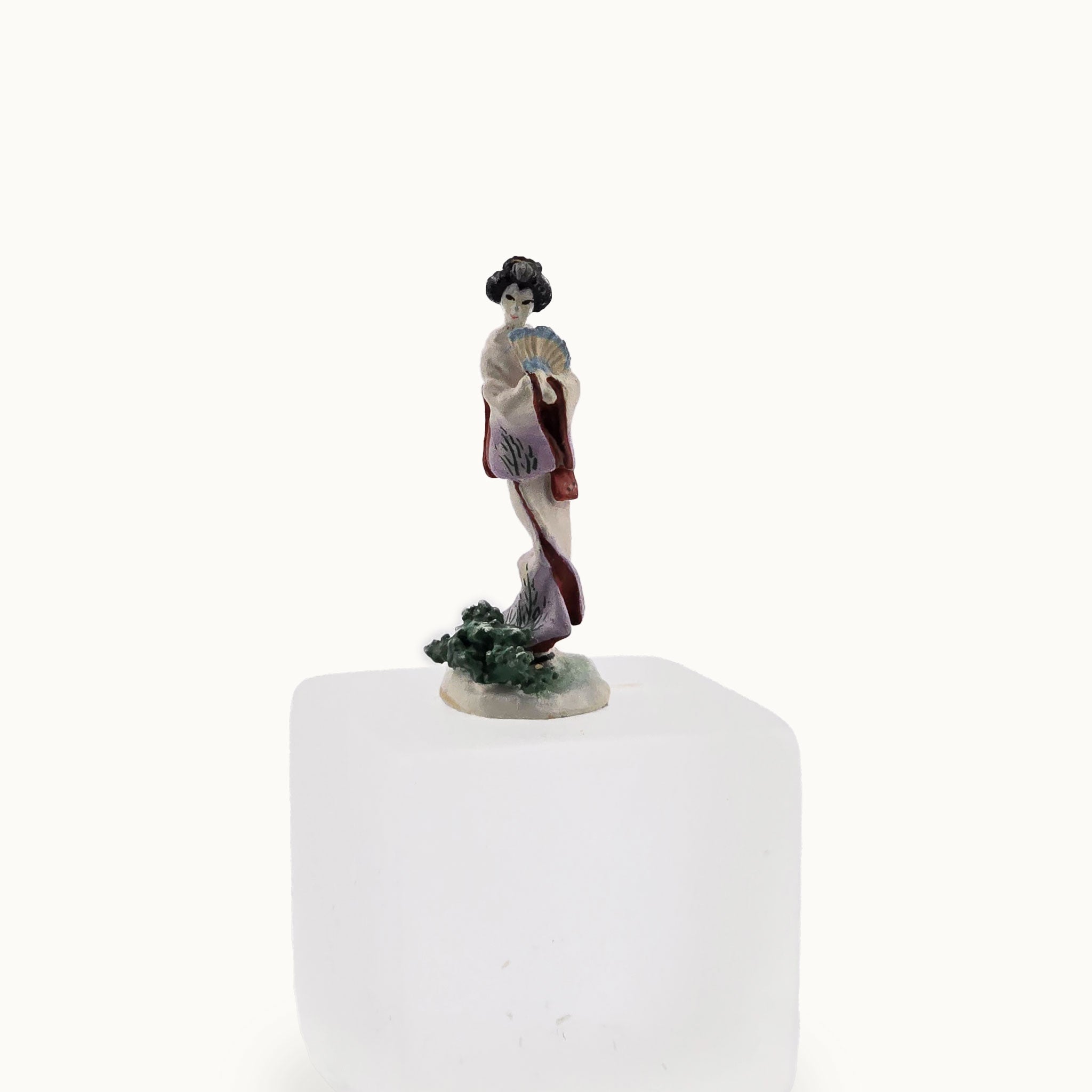 Porcelain figurine of a traditional Japanese geisha on a white pedestal with a white background