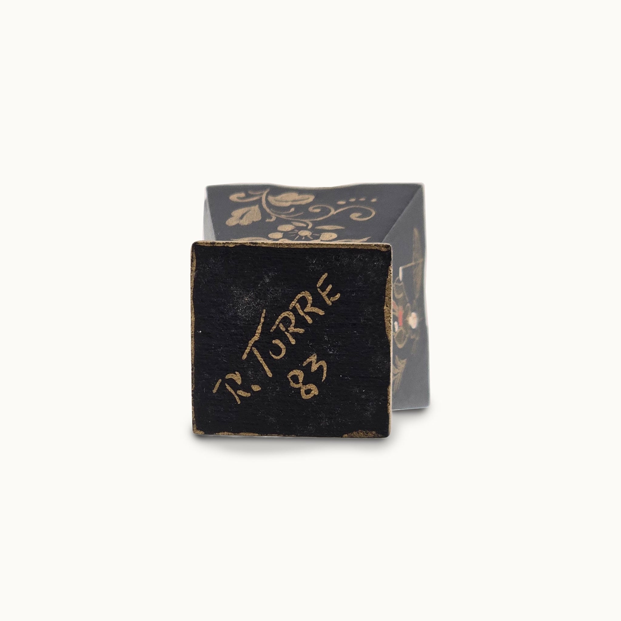 Black decorative box with gold text on a white background, the signature of Artist Rosemarie Torre, dated 1983.